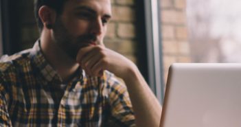 A photo of a person in a cafe contemplating what is on their computer screen